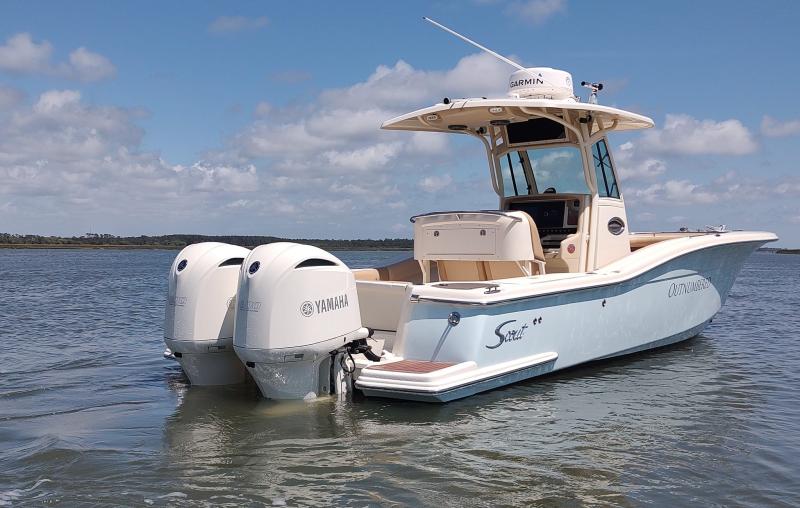 Baby blue scout boat with white outboard motors on the water on a cloudy day